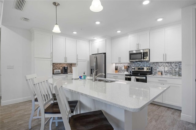 kitchen with pendant lighting, stainless steel appliances, light wood-type flooring, and white cabinets