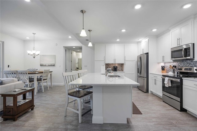 kitchen with appliances with stainless steel finishes, sink, pendant lighting, and an island with sink