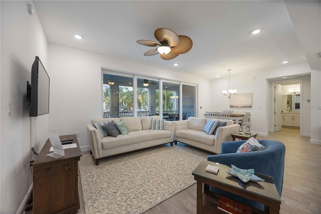 living room featuring ceiling fan with notable chandelier and light hardwood / wood-style flooring