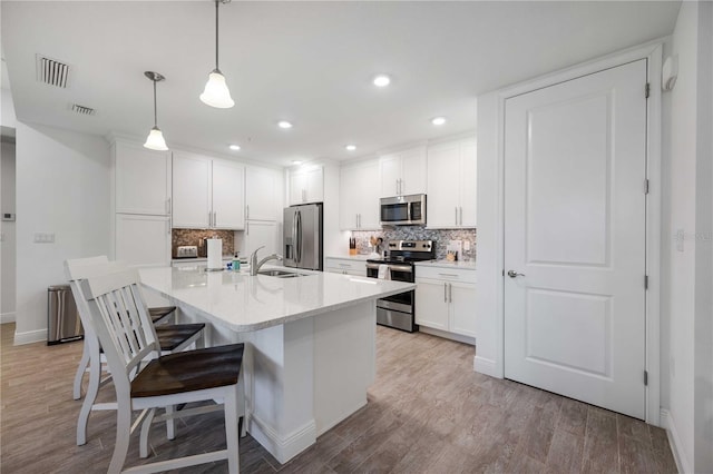 kitchen featuring white cabinets, backsplash, pendant lighting, stainless steel appliances, and light hardwood / wood-style flooring