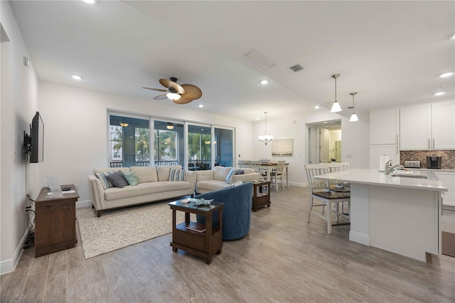 living room with ceiling fan with notable chandelier, sink, and light hardwood / wood-style flooring