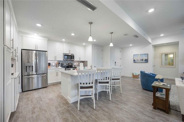 kitchen with hanging light fixtures, a center island with sink, white cabinetry, stainless steel appliances, and light wood-type flooring