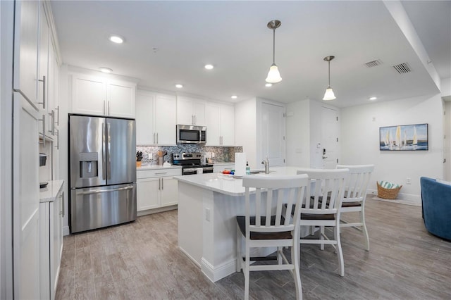 kitchen with white cabinetry, stainless steel appliances, light hardwood / wood-style flooring, decorative light fixtures, and a center island with sink