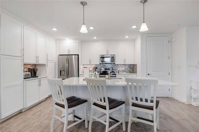 kitchen with white cabinetry, appliances with stainless steel finishes, hanging light fixtures, and a kitchen island with sink