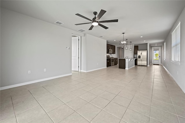 unfurnished living room featuring ceiling fan with notable chandelier, sink, and light tile patterned floors