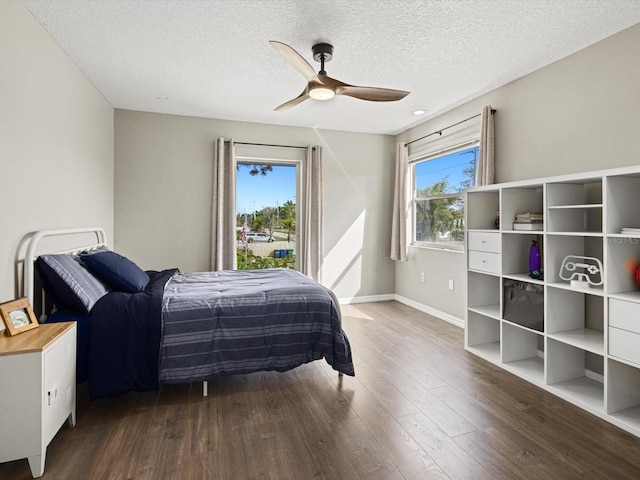 bedroom with ceiling fan, a textured ceiling, multiple windows, and dark hardwood / wood-style flooring