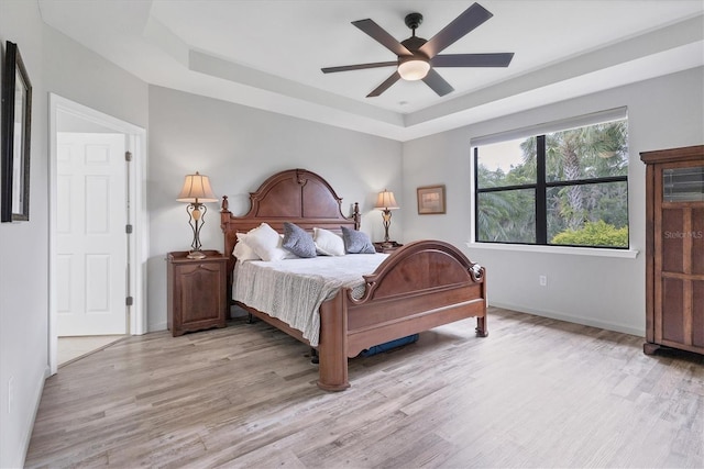 bedroom with ceiling fan, a tray ceiling, and light hardwood / wood-style flooring