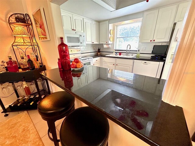 kitchen with light tile patterned floors, white appliances, white cabinets, and a kitchen bar