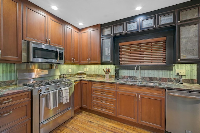 kitchen featuring decorative backsplash, appliances with stainless steel finishes, light wood-type flooring, sink, and dark stone countertops