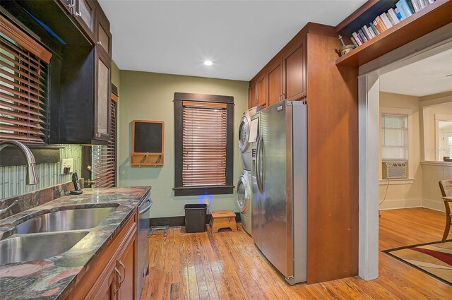 kitchen with sink, dark stone counters, appliances with stainless steel finishes, stacked washer and clothes dryer, and light wood-type flooring