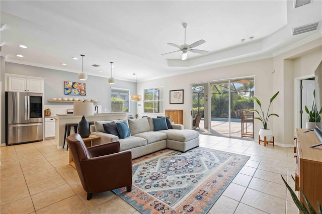 living room with ceiling fan, light tile patterned floors, ornamental molding, and a raised ceiling