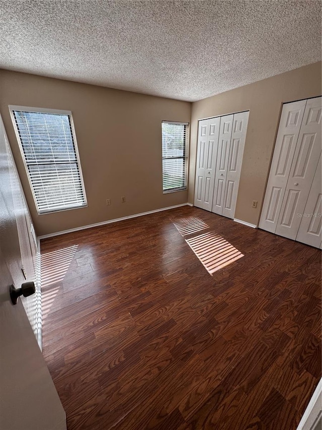 unfurnished bedroom with dark hardwood / wood-style floors, a textured ceiling, and two closets