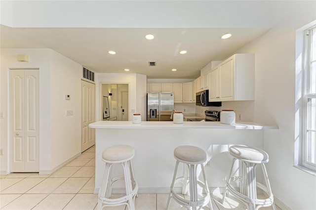 kitchen featuring kitchen peninsula, a kitchen breakfast bar, stainless steel appliances, white cabinets, and light tile patterned floors