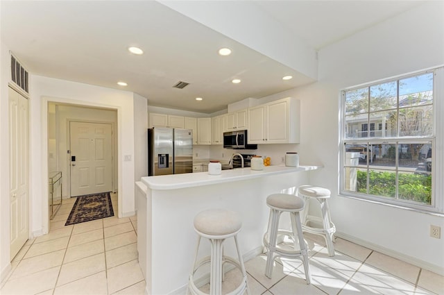 kitchen featuring a kitchen breakfast bar, kitchen peninsula, sink, light tile patterned floors, and appliances with stainless steel finishes