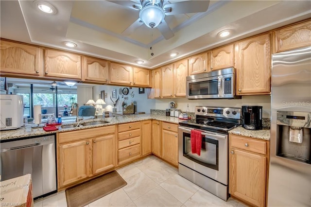 kitchen with ceiling fan, sink, appliances with stainless steel finishes, a tray ceiling, and light brown cabinetry