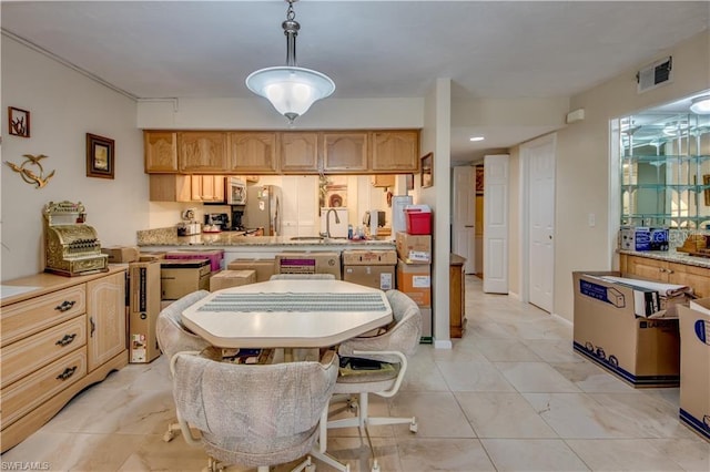 kitchen with light brown cabinetry, hanging light fixtures, and sink