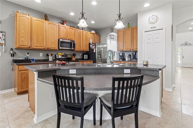 kitchen featuring appliances with stainless steel finishes, hanging light fixtures, an island with sink, light tile patterned floors, and sink