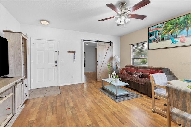 living room with light hardwood / wood-style floors, ceiling fan, and a barn door