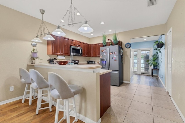 kitchen with kitchen peninsula, decorative light fixtures, light hardwood / wood-style flooring, stainless steel appliances, and a kitchen breakfast bar