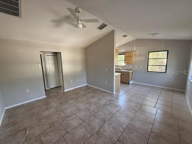 spare room with vaulted ceiling, a textured ceiling, visible vents, and a ceiling fan