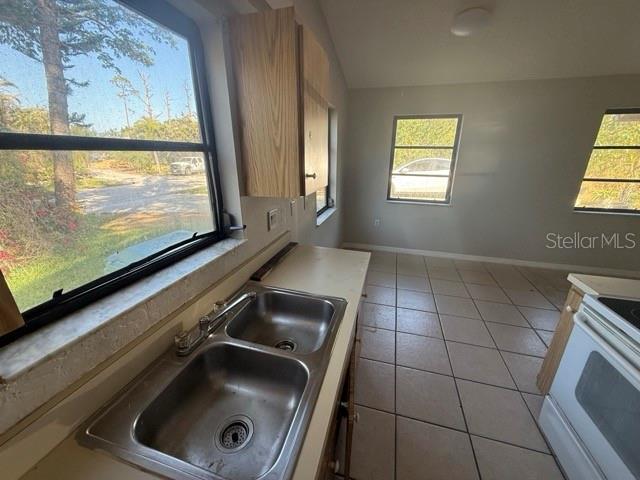 kitchen featuring white electric stove, baseboards, light countertops, a sink, and light tile patterned flooring