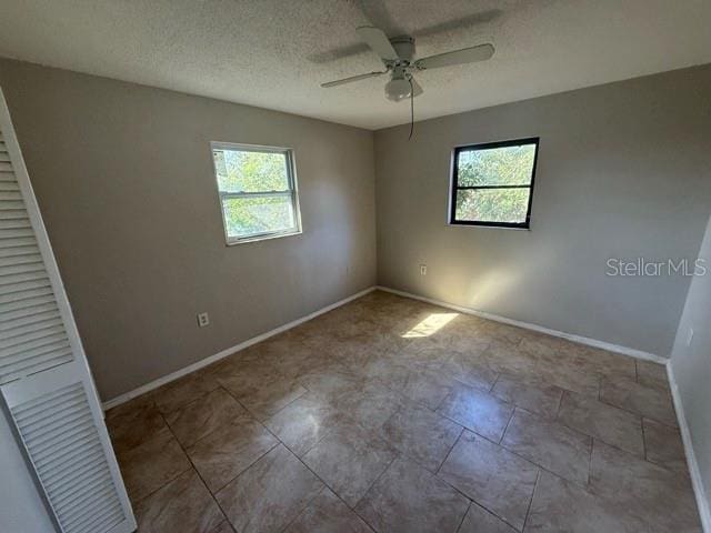 empty room with ceiling fan, baseboards, and a textured ceiling