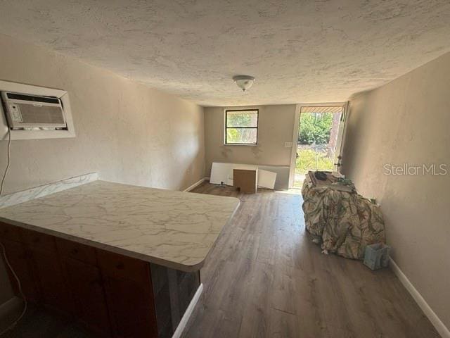 interior space featuring baseboards, wood finished floors, light countertops, a textured ceiling, and an AC wall unit