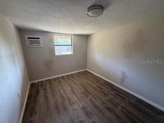 spare room with baseboards, dark wood-type flooring, a textured ceiling, and a wall mounted air conditioner