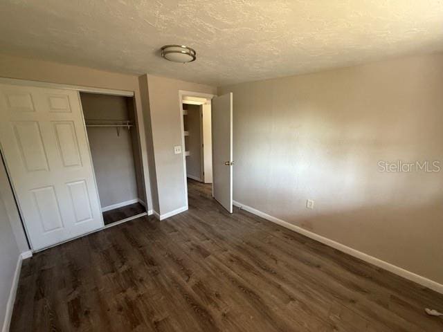 unfurnished bedroom with a textured ceiling, baseboards, dark wood-type flooring, and a closet