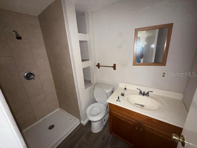 full bathroom featuring toilet, wood finished floors, tiled shower, and vanity