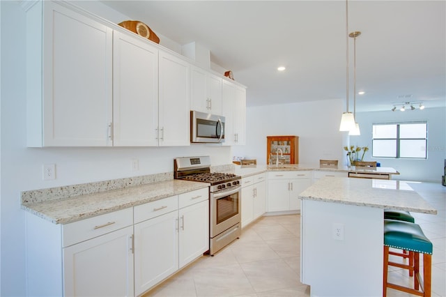 kitchen featuring hanging light fixtures, kitchen peninsula, white cabinetry, appliances with stainless steel finishes, and a breakfast bar