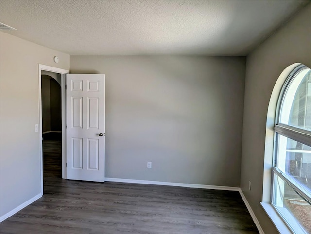 spare room featuring plenty of natural light, a textured ceiling, dark wood-type flooring, and baseboards