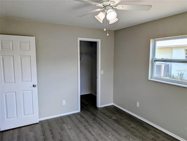 unfurnished bedroom featuring wood finished floors, baseboards, a closet, ceiling fan, and a walk in closet