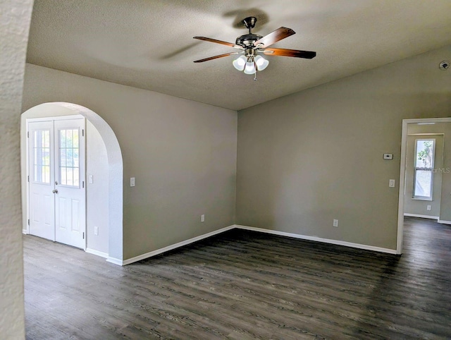 empty room featuring arched walkways, dark wood-style flooring, a ceiling fan, a textured ceiling, and baseboards