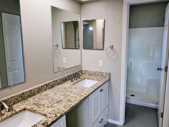 bathroom featuring tile patterned flooring, a stall shower, double vanity, and a textured wall