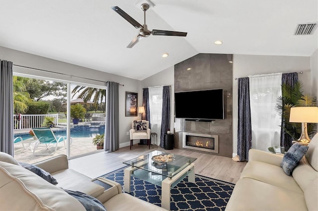 living room with a tiled fireplace, vaulted ceiling, hardwood / wood-style floors, and ceiling fan