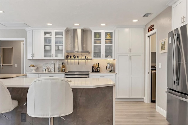 kitchen featuring appliances with stainless steel finishes, a breakfast bar, wall chimney range hood, and white cabinets