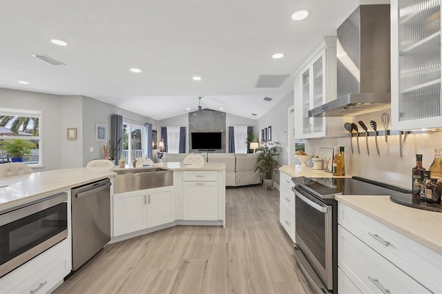 kitchen featuring appliances with stainless steel finishes, white cabinetry, lofted ceiling, sink, and wall chimney range hood