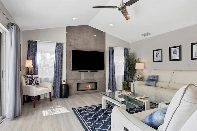 living room featuring a fireplace, vaulted ceiling, light hardwood / wood-style floors, and ceiling fan