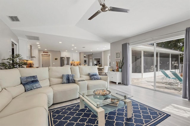 living room with ceiling fan, light hardwood / wood-style floors, and vaulted ceiling