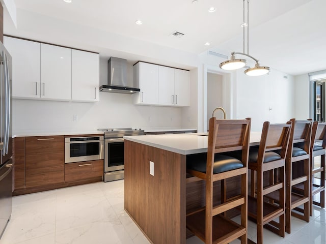 kitchen with pendant lighting, a center island, wall chimney range hood, white cabinetry, and stainless steel appliances