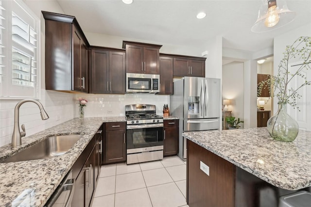 kitchen featuring light stone counters, dark brown cabinetry, sink, stainless steel appliances, and decorative backsplash