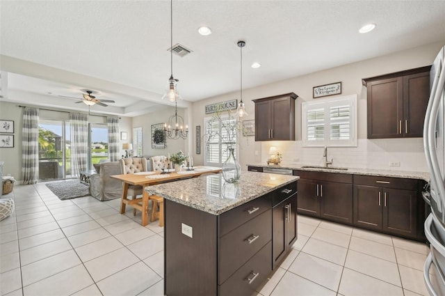 kitchen featuring sink, ceiling fan with notable chandelier, hanging light fixtures, a kitchen island, and dark brown cabinetry