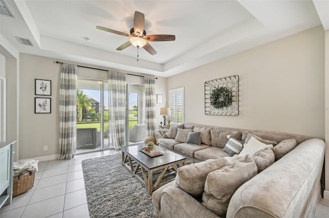 tiled living room with ceiling fan, a raised ceiling, and a healthy amount of sunlight