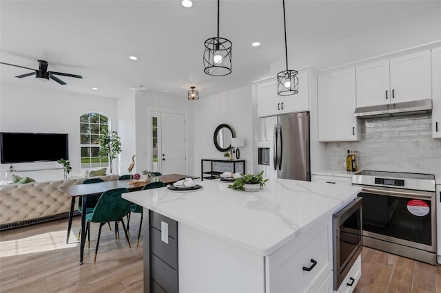 kitchen with appliances with stainless steel finishes, tasteful backsplash, decorative light fixtures, white cabinets, and a kitchen island