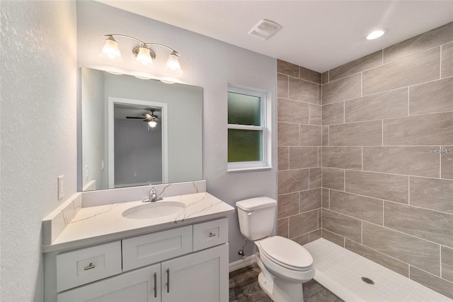 bathroom featuring a tile shower, vanity, toilet, and ceiling fan