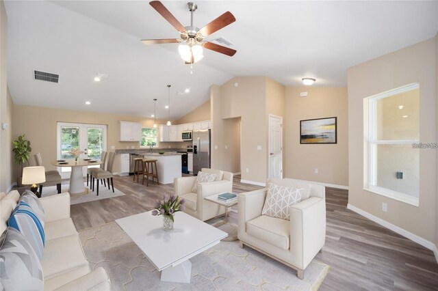 living room with light wood-type flooring, vaulted ceiling, sink, and ceiling fan