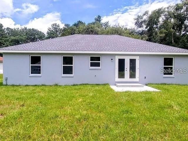 6319 NW 67th Ter, Ocala, FL 34482 - rear view of house featuring stucco siding, a shingled roof, a yard, and french doors