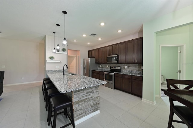 kitchen featuring hanging light fixtures, light stone countertops, sink, backsplash, and appliances with stainless steel finishes