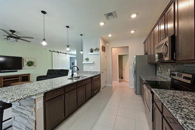 kitchen with hanging light fixtures, light stone countertops, sink, appliances with stainless steel finishes, and a breakfast bar area